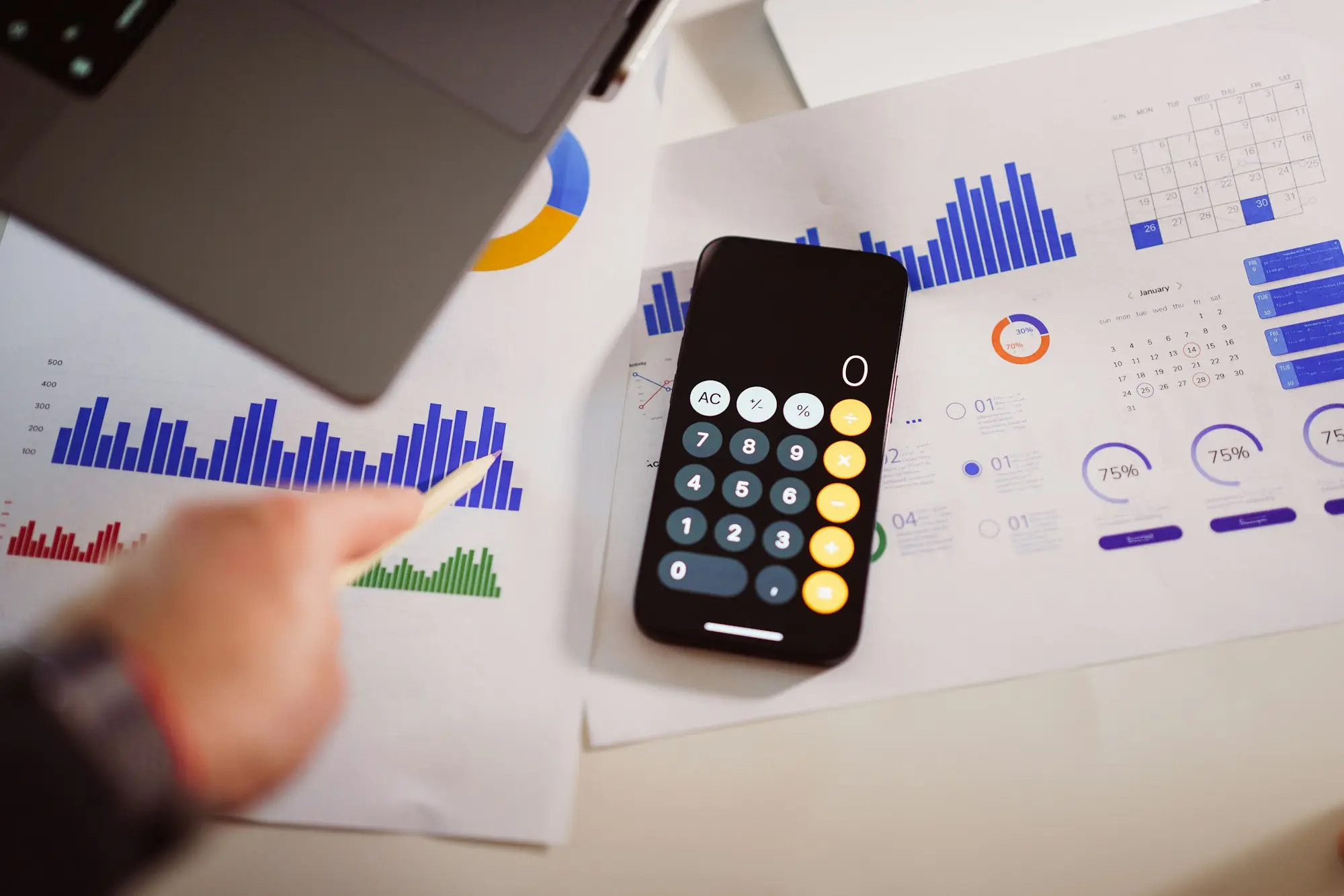 Calculator and laptop on a desk with financial charts